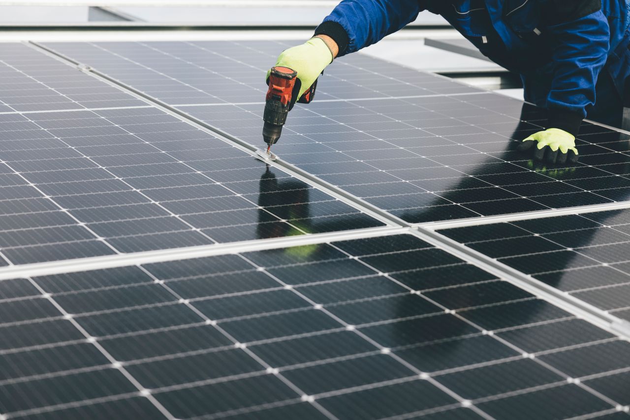 A technician uses a power tool to install solar panels, showcasing renewable energy efforts.